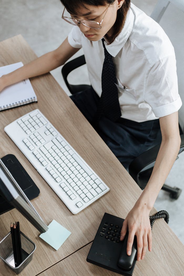 Asian woman in corporate attire working at office desk with phone and computer.
